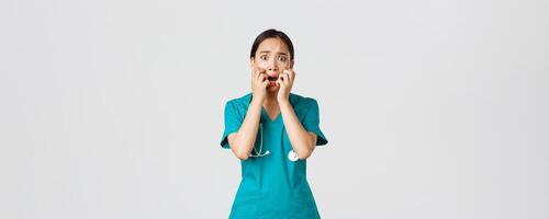 covid19, sjukvård arbetare och förebyggande virus begrepp. rädd osäker asiatisk kvinna läkare, sjuksköterska i scrubs börjar till panik från rädsla, bitande fingernaglar och ser förskräckt, vit bakgrund foto