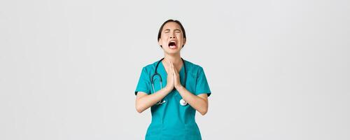 covid19, sjukvård arbetare, pandemi begrepp. överarbetad ledsen och trött asiatisk kvinna läkare, sjuksköterska tiggeri för hjälp, inlagan Gud och gråt från påfrestning, stående vit bakgrund foto