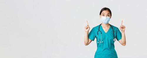 covid19, coronavirus sjukdom, sjukvård arbetare begrepp. fascinerad och upphetsad asiatisk kvinna läkare, sjuksköterska i medicinsk mask och handskar, ser och pekande fingrar upp, vit bakgrund foto