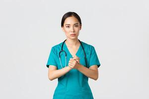 covid19, sjukvård arbetare, pandemi begrepp. hoppfull seriöst utseende asiatisk sjuksköterska, läkare be något med bekymrad ansikte, knyta händer tillsammans i Stöd under coronavirus, vit bakgrund foto