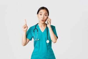 covid19, sjukvård arbetare och förebyggande virus begrepp. porträtt av skön asiatisk kvinna läkare, sjuksköterska i scrubs talande på telefon och höja finger som ha bra aning, kom ihåg, föreslå planen foto