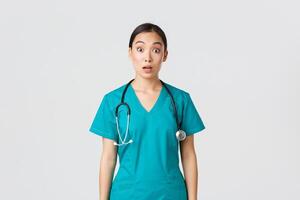 covid19, sjukvård arbetare, pandemi begrepp. imponerad och överraskad asiatisk sjuksköterska i scrubs släppa käke och stirra på kamera mållös, ser förvånad över vit bakgrund foto