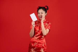 Lycklig kinesisk ny år, upphetsad ung asiatisk kvinna bär röd Cheongsam innehav kreditera kort isolerat på röd bakgrund. foto