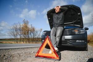 man reparation en bruten bil förbi de väg. man har problem med hans bruten bil på de motorväg vid vägkanten. man ser under de bil huva. bil bryter ner på de autobahn. vid vägkanten bistånd begrepp. foto