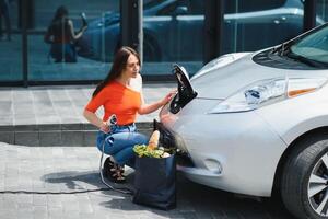 kvinna laddning elektro bil på de elektrisk gas station foto