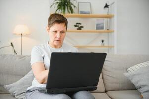 teknologi, människor och kommunikation begrepp - Lycklig senior kvinna med läsplatta pc dator har video chatt på Hem. modern medelålders 50s mormor sitta koppla av på soffa i levande rum använder sig av bärbar dator. foto