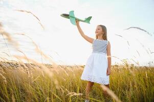 Lycklig flicka kör med en leksak flygplan på en fält i de solnedgång ljus. barn spela leksak flygplan. tonåring drömmar av flygande och passande en pilot. flicka vill ha till bli en pilot och astronaut. långsam rörelse. foto