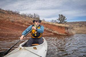 senior manlig i liv jacka är paddling expedition kanot, kall säsong landskap på hästtand reservoar i nordlig colorado, pOV från verkan kamera foto