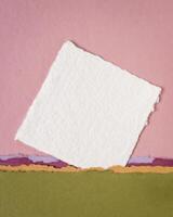 små ark av tom vit khadi trasa papper från Indien mot abstrakt landskap i rosa och grön pastell toner foto
