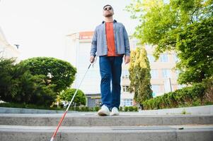 ung blind man med vit sockerrör gående tvärs över de gata i stad foto
