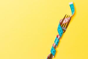 diet och friska äter begrepp med insvept gaffel i mätning tejp på gul bakgrund. topp se av viktminskning med kopia Plats foto
