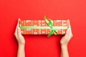 kvinnliga händer innehav randig gåva låda med färgad band på röd bakgrund. jul begrepp eller Övrig Semester handgjort närvarande låda, begrepp topp se med kopia Plats foto