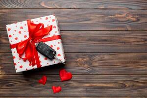 svart bil nyckel i en närvarande låda med en band och röd hjärta på färgad bakgrund. valentine dag sammansättning topp se foto
