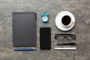 modern kontor skrivbord tabell med anteckningsbok, smartphone och Övrig leveranser med kopp av kaffe. tom anteckningsbok sida för du design. topp se, platt lägga foto