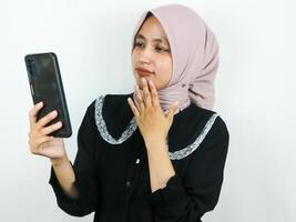 porträtt skön asiatisk kvinna bär hijab, leende medan innehav mobil telefon foto