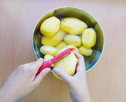 stänga upp av man innehav och peeling potatis. händer skärande potatisar på kök till förbereda en recept. foto