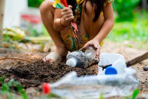 liten flicka plantering växter i kastruller från återvunnet vatten flaskor i de bakgård. återvinna vatten flaska pott, trädgårdsarbete aktiviteter för barn. återvinning av plast avfall foto