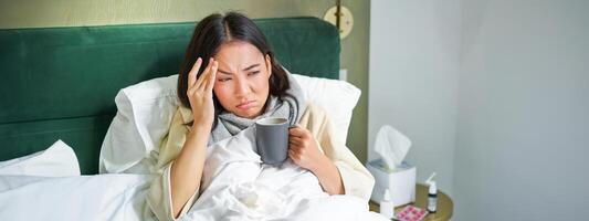influensa, sjukdom och människor. ung kvinna känsla sjuk, har feber och fångst col, liggande i säng med varm te, tar läkemedel från influensa foto