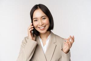 leende företags- kvinna i kostym, talande på mobil telefon, har en företag ring upp på smartphone, stående över vit bakgrund foto