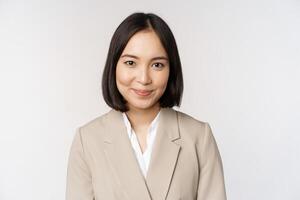 stänga upp porträtt av affärskvinna, asiatisk kvinna entreprenör i kostym, leende och ser professionell, stående mot vit bakgrund foto