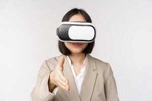 möte i vr chatt. asiatisk affärskvinna i virtuell verklighet glasögon, förlängning hand för handslag med företag partner, hälsning någon, stående över vit bakgrund foto