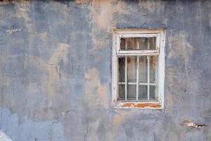 gammal fönster med en trä- ram och en gitter i en lila vägg med beige fläckar. skalad vit måla på de ram. foto