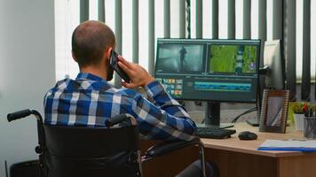 Inaktiverad frilansare videographer talande på telefon under redigering en video projekt skapande innehåll Sammanträde i rullstol i modern företag kontor. skapare bloggare arbetssätt från Foto studio.