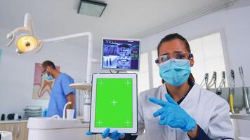 tandläkare läkare som visar läsplatta med grön skärm, förklara dental radiografi och diagnos för tänder infektion. stomatologi specialist med ansikte mask pekande på mockup, kopia Plats, krom visa foto