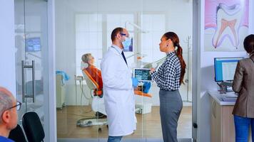 tandvård läkare som visar röntgen av tänder till patient använder sig av läsplatta stående i väntar område av dental klinik . stomatolog granskning dental radiografi med kvinna förklara behandling i fullt med folk kontor foto
