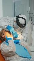 tandläkare med ansikte skakade behandla tänder till senior kvinna patient i dental klinik under covid-19 . läkare och sjuksköterska arbetssätt bär overall, skydd kostym, mask, handskar i stomatologisk kontor. foto
