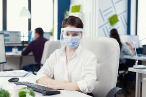 kvinna entreprenör bär ansikte mask mot covid19 som säkerhet försiktighetsåtgärd på arbetsplats företag team arbetssätt i finansiell företag respekterar social distans under global pandemisk. foto