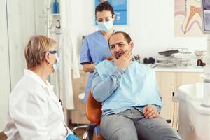 stomatolog läkare talande till man patient med tandvärk Sammanträde på dental stol framställning för medicinsk undersökning. tandläkare team arbetssätt i stomatologi sjukhus klinik kontor foto