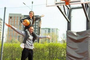 Lycklig far och tonåring dotter utanför på basketboll domstol. foto