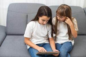 chockade systrar använder sig av digital läsplatta på soffa på Hem foto