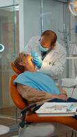 läkare granskning tänder med medicinsk instrument arbetssätt med handskar i modern tandläkare klinik. ortodontist tala till kvinna Sammanträde på stomatologisk stol medan sjuksköterska framställning verktyg för undersökning foto