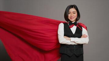 asiatisk receptionist Framställ med röd superhjälte cape på kamera, känsla självsäker och kraftfull medan hon bär en dölja som en hjälte. hotell concierge operatör stående med vapen korsade. kamera a. foto