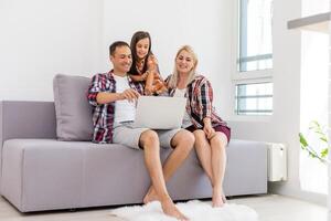 Lycklig familj använder sig av bärbar dator tillsammans på soffa i hus foto