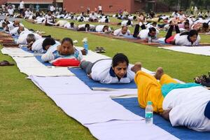 ny delhi, Indien, juni 21, 2023 - grupp yoga övning session för människor på yamuna sporter komplex i delhi på internationell yoga dag, stor grupp av vuxna delta yoga klass i cricket stadion foto