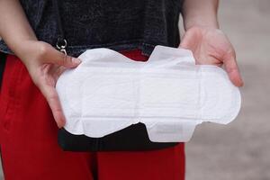 stänga upp kvinna hand är innehav sanitär servett. begrepp, kvinnliga hygienisk produkt för period dag. menstruations- smärta på de dag av period. kvinna sjukvård. en gång i månaden intim hygien. foto