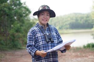 asiatisk kvinna explorer håll papper Karta till utforska natur på skog och sjö område. begrepp, natur utforskning. ekologi studie. tidsfördriv aktivitet, livsstil. utforska miljö foto
