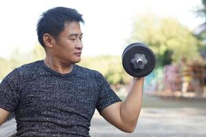 stilig asiatisk man övningar utomhus, hiss hantel. begrepp, övning för hälsa bodybuilding. stärka muskel. vikt lyft. friska livsstil. sport Utrustning. arbete ut gör stark av kropp. foto