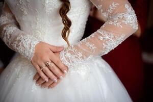 detaljer av skön spets bröllop klänning och honor händer med gyllene ringar. stänga upp på en brud händer och vit klänning för bröllop. foto