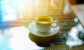 en kopp av kaffe i de morgon- i de Sol på en glas tabell foto