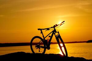 cykel bredvid vatten med solnedgång. aktiva livsstil begrepp foto