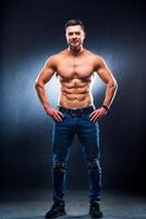 atletisk kroppsbyggare med naken torso Framställ med händer på midja. studio Foto. full storlek porträtt av en stilig man i jeans. foto