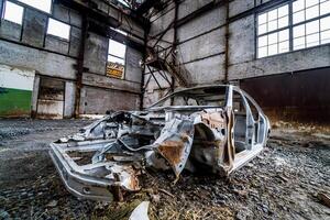 ruttnande bil i övergiven fabrik. interiör av ett övergiven fabrik med gammal maskineri foto