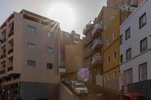 Sol blossa över urban gata med modern lägenhet byggnader och parkerad bilar, skildrar stad levande i los cristianos, teneriffa. foto