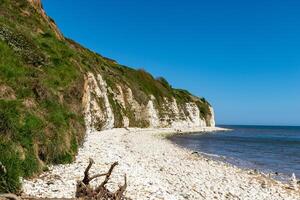 naturskön se av en vit krita klippa förbi de hav med en sten strand under en klar blå himmel. foto