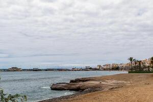 lugn strandlandskap med molnig himmel, lugna hav, och kust stad i de bakgrund i los cristianos, teneriffa. foto