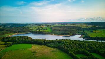 antenn se av en lugn sjö omgiven förbi frodig grönska och fält under en blå himmel med spridd moln i yorkshire. foto